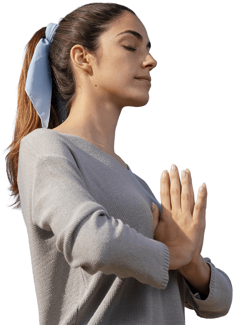 A woman in a gray sweater stands with her hands together, wearing a light blue scarf in her hair.